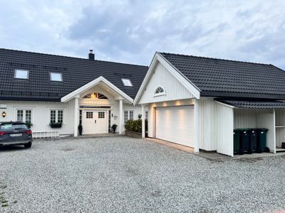 Fotografi av en hvit villa med garasje og kjørevei.