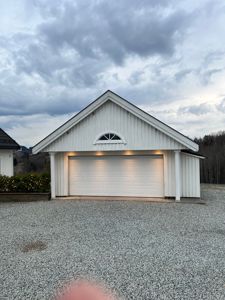 Fotografi av en hvit garasje med gavl og et vindue i fronten, sett fra foran.