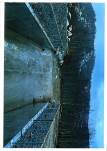 Fotografi av en byggeplass som viser en betongfundamentmur, grus og en skogbakke.