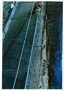 Fotografi av en ferdig eller under bygging fasade med betongmur, hekk og terreng.