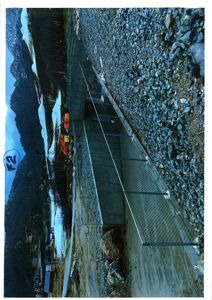 Fotografi av en byggeplass med en ferdigbetont bro eller tunnelport i bakgrunnen, omgitt av fjell og grus.