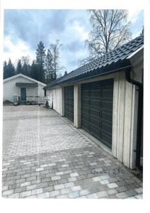 Fotografi av en garasje med grå port, forplass med flislagt gulv og en annen bygning i bakgrunnen.