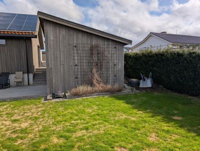 Fotografi av en bakgård med en uthusbygning, solcellepaneler på taket og en hage.