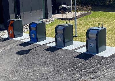 Fotografi av fire sorteringsskap (godsbeholdere) plassert utenfor en bygning på en asfaltert overflate.