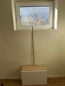 Fotografi av en vegg med et vindu og et lite skap eller benk foran. En målebånd er plassert vertikalt for å vise høyde.