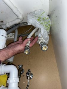 Fotografi av rørleggerarbeid under en vask, med en hånd som holder på vannledninger.