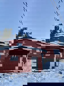 Fotografi av en rød bygning med hvit dør og vinduer, sett fra front med snø på bakken.