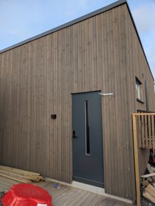 Fotografi av en ferdig eller nesten ferdig bygning sett fra utsiden, med fokus på fasaden, dør og omgivelser.