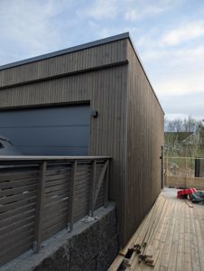 Fotografi av en ferdig eller nesten ferdig bygning med trepanel, garasjeport og uteplass.