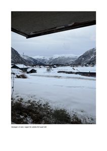 Fotografi av utsikt fra en garasje (eller vindu) mot en snødekt dal med fjell og hus i bakgrunnen.