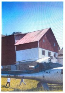 Fotografi av en rød og hvit bygning med et helikopter i forgrunnen.