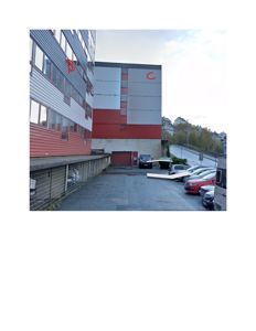 Fotografi av en bygning sett fra utsiden, med parkerte biler i forgrunnen og nabolag i bakgrunnen.