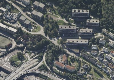 Flyfoto eller satellittbilde som viser et boligområde med flere bygninger, veier og grøntområder.