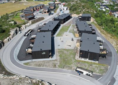 Fotografi av et byggprosjekt under oppføring sett fra luften, som viser flere mørke bygninger på en kupert tomt.