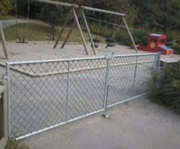 Fotografi av en gate med en metallgjerdeport og et lekeplassområde med svang og rødt leketøy i bakgrunnen.