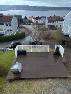 Fotografi av en ferdig montert terrasse med hvit hekk, sett fra et høyere nivå mot havet.