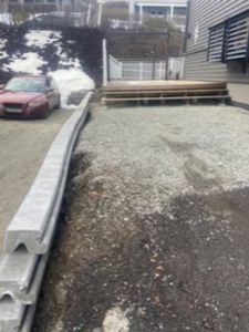 Fotografi av en byggeplass eller uteområde med grus, betongelementer og en bil.