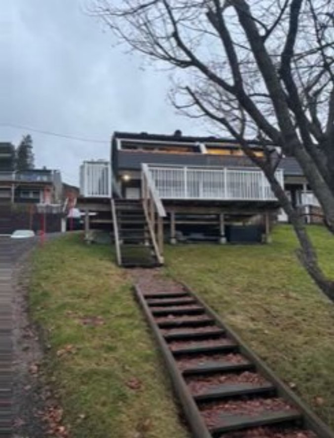 Fotografi av en moderne villa sett fra siden, med trapper opp til etasjen og en grønn hage.