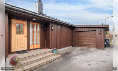 Fotografi av fasaden på en enebolig med garasje, inkludert inngangsdør, vinduer og husnummer.