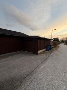 Fotografi av en mørkebrun garasje med tak og en vei i forgrunnen.