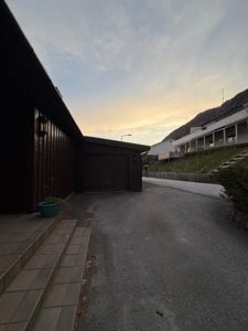 Fotografi av en bolig med garasje, trapp og vei, sett fra gaten mot huset.