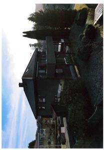 Fotografi av en eksisterende bolig sett fra siden, med trær og naboegenskaper i bakgrunnen.