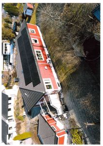 Luftfoto av en bolig med solcellepaneler på taket og omgivende hage.