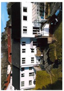 Fotografi av en hvit bolig med etasje og terrasse sett fra siden.