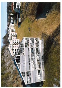 Fotografi av en moderne bygning med glassfasade, sett fra luft eller høyde, med nabolag i bakgrunnen.