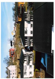 Fotografi av en bebygd skråning med flere hus og en blå himmel.