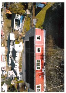 Luftfoto av en rød og hvit bygning med solceller på taket, sett fra høyden.