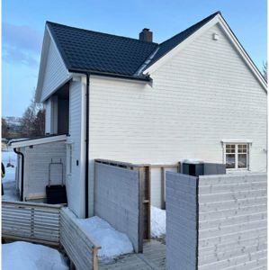 Fotografi av en hvit, moderne villa under bygging eller renovering, med snø på bakken og delvis ferdig fasade.