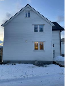 Fotografi av en hvit, toetasjes bolig sett fra siden, med snø på bakken og lys i vinduene.