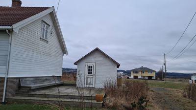 Fotografi av en hvit hytte med etasjehus i bakgrunnen.