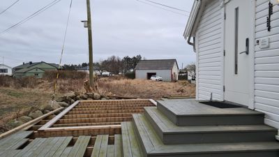 Fotografi av en uteplattform under bygging eller renovering, med trapp opp til en hvit bygning.