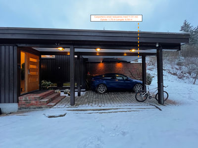 Fotografi av en eksisterende eller ferdigstilt bygning med carport, bil og sykkel i snø. Bildet inneholder også en annotasjon som viser en beregning av carportens areal.