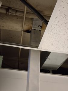 Fotografi av et takrom eller loft med synlige rør, en hvit gipsplater (kassetter) og en metallbjelke.