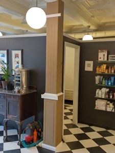 Fotografi av et interiør, sannsynligvis en salong eller butikk, med sjakkfliser på gulvet, mørke vegger og en søylen.