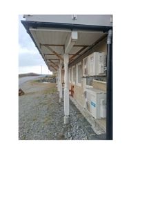 Fotografi av en bygning sett fra siden, som viser etasjens takoverheng med søyler, fasade med vinduer og utendørs klimaanlegg.