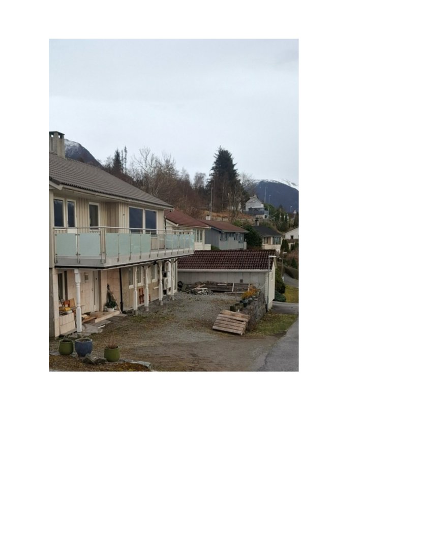 Fotografi av en toetasjes bolig med balkong, garasje og omgivelser i et fjellområde.