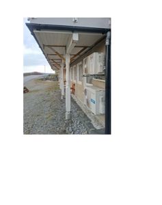 Fotografi av en bygning sett fra siden, som viser etasjens takoverheng med søyler, fasade med vinduer og utendørs klimaanlegg.