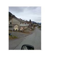 Fotografi av en eksisterende bolig med garasje og hage sett fra veien.