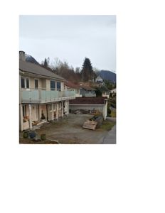 Fotografi av en toetasjes bolig med balkong, garasje og omgivelser i et fjellområde.