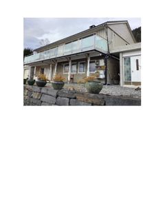 Fotografi av en eksisterende bygning sett fra bak/side, med balustrade og hageelementer i forgrunnen.