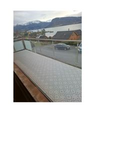 Fotografi tatt fra en balkong eller terrasse som viser utsikt over et boligområde med fjord og fjell i bakgrunnen.