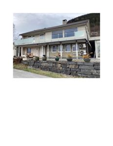 Fotografi av en toetasjes bolig med balkong, vinduer og steinmur foran.