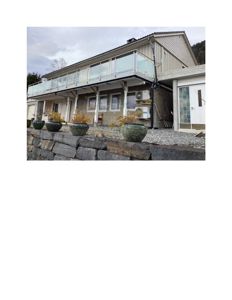 Fotografi av en eksisterende eller ferdigstilt bolig sett fra siden, med fokus på fasade, balkong og hage.