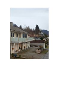 Fotografi av en toetasjes bolig med balkong, garasje og omgivelser inkludert fjell i bakgrunnen.