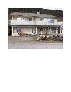 Fotografi av en toetasjes bolig under ombygging eller nybygging, med synlig fasade, balkong og omgivelser.