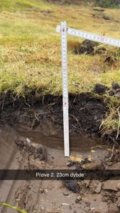 Fotografi av et jordprøvetaking med målestokk som viser dybde på 23 cm.